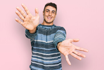 Hispanic young man wearing casual clothes looking at the camera smiling with open arms for hug. cheerful expression embracing happiness.