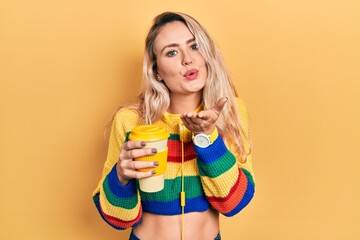 Sticker - Beautiful young blonde woman drinking cup of coffee wearing headphones looking at the camera blowing a kiss with hand on air being lovely and sexy. love expression.