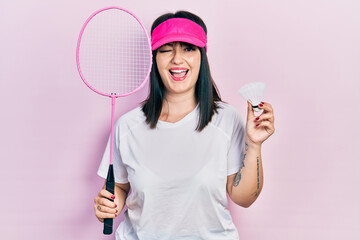 Canvas Print - Young hispanic woman holding badminton racket and shuttlecock winking looking at the camera with sexy expression, cheerful and happy face.