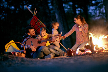 Wall Mural - A young happy family having playing around a campfire in the forest
