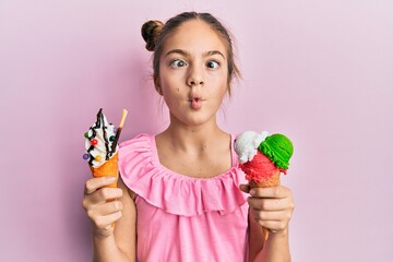 Beautiful brunette little girl eating ice cream cones making fish face with mouth and squinting eyes, crazy and comical.