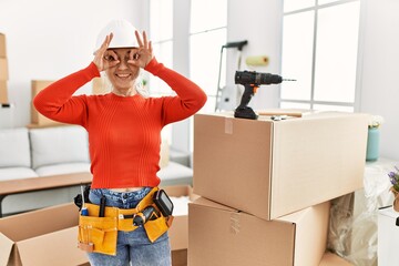 Canvas Print - Middle age grey-haired woman wearing hardhat standing at new home doing ok gesture like binoculars sticking tongue out, eyes looking through fingers. crazy expression.