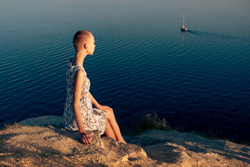 Wall Mural - teenager girl in a short haired dress sitting on a cliff over a sea, looking at the ship