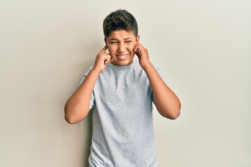 Poster - Teenager hispanic boy wearing casual grey t shirt covering ears with fingers with annoyed expression for the noise of loud music. deaf concept.