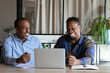 Excited two African American employees working on online project together, looking at laptop screen, discussing sharing ideas or funny news, brainstorming at meeting in office, teamwork concept