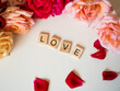 LOVE - napis z drewnianych kostek, róże w tle, różowy kolor