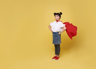 Little child asian girl plays superhero on yellow background studio shot. Girl power hero concept.