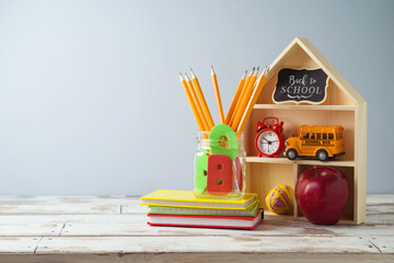 Back to school concept with pencils, notebook and toy house on wooden table.