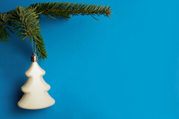 a white glass christmas toy in the form of a christmas tree hangs on a green branch of a christmas t