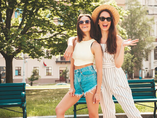 Two young beautiful smiling hipster female in trendy summer clothes.Sexy carefree women posing on the street background in hat. Positive pure models having fun at sunset, hugging