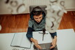 © Minet - Top view, the little boy using laptop and headphones studying math during his online lesson at home, social distance during quarantine, self-isolation. takes notes.