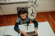 © Minet - Top view, the little boy using laptop and headphones studying math during his online lesson at home, social distance during quarantine, self-isolation. takes notes.