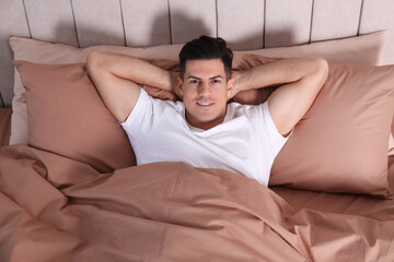 Wall Mural - Man lying in comfortable bed with beige linens, above view