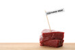 Pieces of raw cultured meat with toothpick label on wooden table against white background