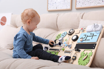 Wall Mural - Cute little boy playing with busy board on sofa at home