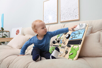 Wall Mural - Cute little boy playing with busy board on sofa at home