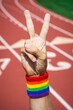Athlete with gay pride rainbow wrist sweatband making a v-sign for victory with hand at a running track