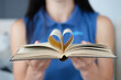 Woman is holding book with a page in shape of heart folded in center