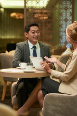 Positive businessman and businesswoman meeting at restaurant table and talking about project they are working on or investment opportunities