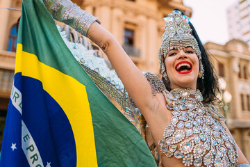 Beautiful Brazilian woman wearing colorful Carnival costume and Brazil flag during Carnaval street parade in city.