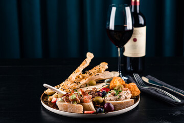 Wall Mural - Italian antipasti wine snacks set. Brushettas, cheese variety, Mediterranean olives and wine in glasses over black grunge background