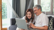 © tirachard - Asian senior couple video call at home. Asian Senior Chinese grandparents, using laptop video call talking with family grandchild kids while lying on sofa in living room at home concept.