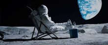 Back View Of Lunar Astronaut Opens A Beer Bottle While Resting In A Beach Chair On Moon Surface, Enjoying View Of Earth