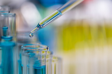 Drop of blue liquid from droper droping to test tube in laboratory with bright color blur background