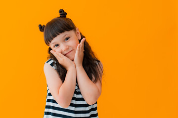 Portrait of happy excited amazed touching gesture with his hands to his face cheeks kid child girl brunette striped dress isolated yellow background