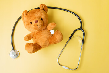 Stethoscope with Bear doll on yellow background for supporting kid living and illness. September Childhood Cancer Awareness month, healthcare and life insurance concept