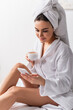 © LIGHTFIELD STUDIOS - happy woman in towel on head and bathrobe using smartphone and holding cup of coffee in bedroom