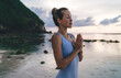 Calm young woman in sportive tracksuit doing harmony exercises during evening time for coastline workout, tranquil Caucasian female athlete in namaste enjoying yoga practice for zen relaxing
