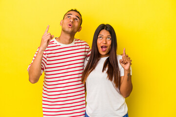 young latin couple isolated on yellow background pointing upside with opened mouth.