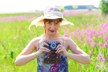 Portrait of a young woman with a camera in a hat in a field of red flowers on a hot summer day. Selective focus. Close-up