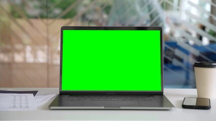 Workplace with laptop computer on desk with blank empty green mockup screen for advertising standing in modern contemporary office. Business software website ads technology concept.