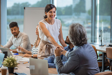 Wall Mural - Two business people shaking hands while sitting in meeting room. Businesswoman shake hands to businessman. Portrait of happy smiling woman signing off deal with an handshake.