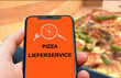 © keBu.Medien - Person hält Smartphone mit einer Pizza-Lieferservice App vor einer Pizza im Karton, Lieferdienst, Lieferservice, Essen, Gastronomie