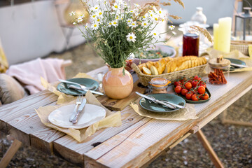 Beautifully served wooden table in natural boho style outdoors. Dining table decorated with field flowers, dishes and fresh food