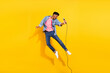 Full length photo of crazy dark skin happy man jump up hold microphone isolated on yellow color background