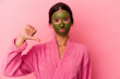 Young caucasian woman wearing a bathrobe and facial mask isolated on pink background showing a dislike gesture, thumbs down. Disagreement concept.