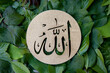 Name of Allah in arabic on gold wood, green leaves background. Calligraphy means the God Al Mighty of Islam Religion.
