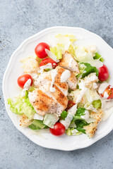 Wall Mural - Caesar salad with grilled chicken breast, cherry tomatoes and lettuce salad topped with traditional caesar salad dressing. Top view