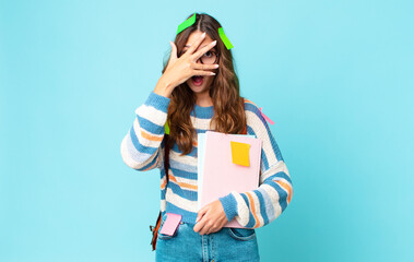 Wall Mural - young pretty woman looking shocked, scared or terrified, covering face with hand with a bag and holding books