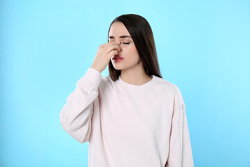 Sticker - Young woman suffering from runny nose on light blue background