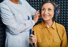 Portrait Senior Woman With White Toothy Smile While Hearing Check-up With ENT-doctor At Soundproof Audiometric Booth Using Audiometry Headphones And Audiometer