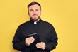 Priest in cassock with Bible on yellow background