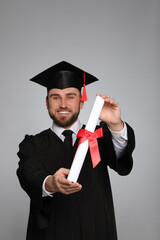 Wall Mural - Happy student with graduation hat against grey background, focus on diploma