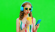 canvas print picture - Summer colorful portrait of stylish young woman listening to music in headphones looking at smartphone and drinking fresh juice on green background