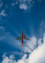 A Passenger Plane From Below Against The Blue Sky And Sun Rays Coming Out Of Clouds. The Aircraft Headed For Landing. Tourists Transportation To A Vacation Place, Trips, Travel Destinations.
