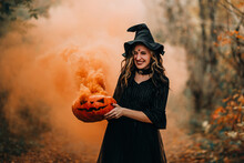 Smiling Girl Dressed As Witch Holding Steaming Pumpkin In Her Hands